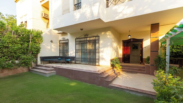 A two-story building with a covered entrance, a bench, and a small garden area.