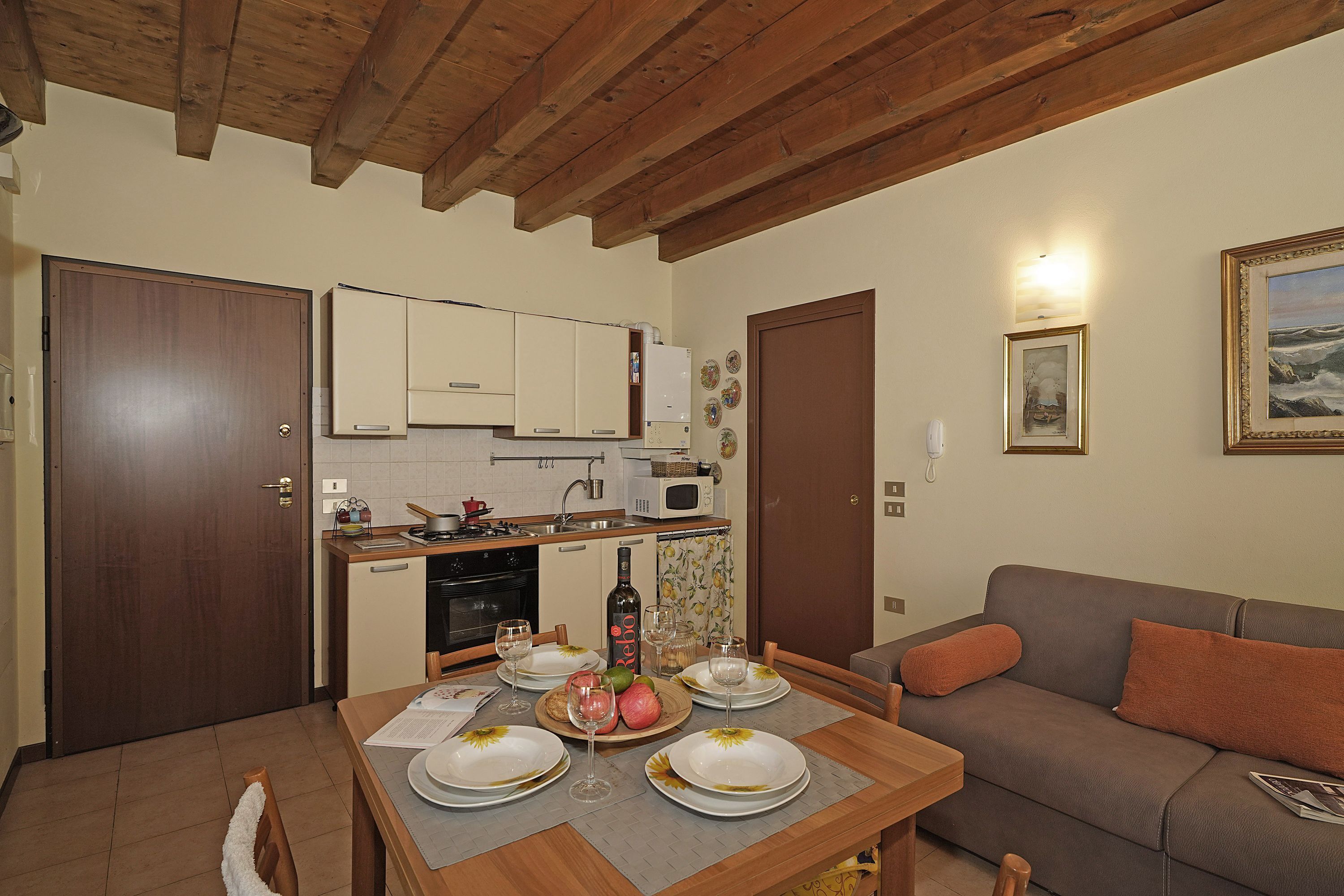 A cozy living room with a wooden ceiling, a brown sofa, and a dining table set for four with plates, glasses, and a bottle of wine.
