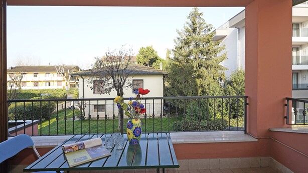 Uma varanda com uma mesa, um vaso de flores e vista para uma área residencial.