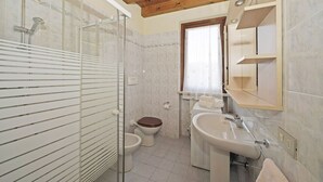 Casa de banho com cabine de chuveiro em vidro, sanita e lavatório com espelho em cima.