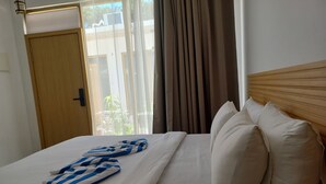 Une chambre d’hôtel avec un lit, une tête de lit en bois, une fenêtre avec des rideaux et une porte.