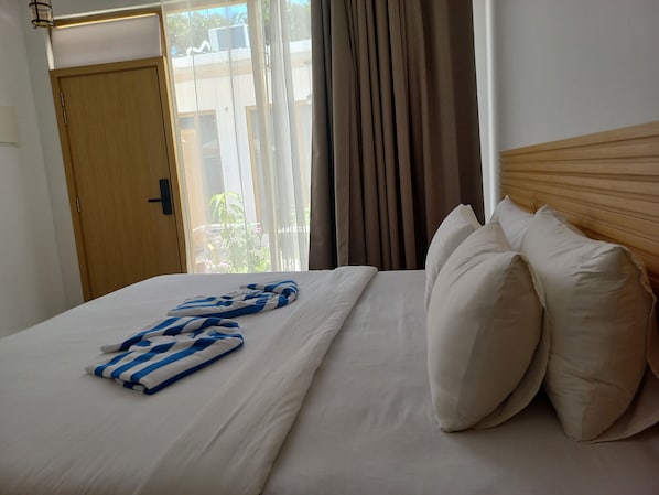 Una habitación de hotel con una cama, cabecera de madera, ventana con cortinas y una puerta.
