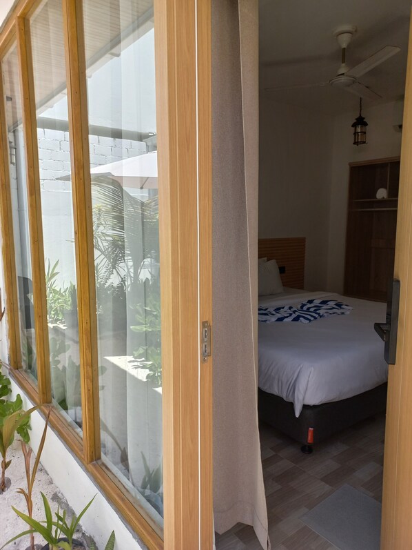 Une chambre à coucher avec un lit, un ventilateur de plafond et une vue sur l’extérieur, visible à travers une porte vitrée.