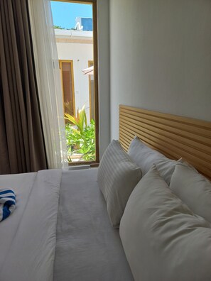 Habitación de hotel con cama, cabecero de madera, ventana con cortinas y vistas al exterior.