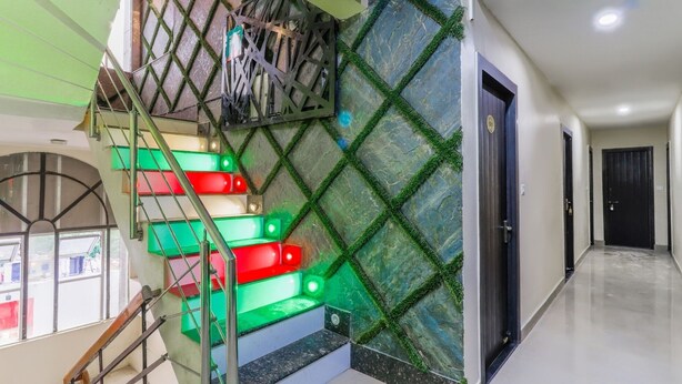A modern staircase with green and red illuminated steps, a metal railing, and a wall with a geometric pattern. - Hotel Mahadeva Regency (Kanpur)