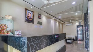 A reception area with a marble counter, framed pictures on the wall, and a ceiling fan. - Hotel Mahadeva Regency (Kanpur)