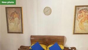 A bedroom with a wooden bed, blue and yellow pillows, a clock on the wall, and two paintings. - Maleth House (Naxxar)