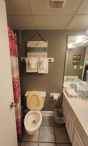 A bathroom with a toilet, a towel rack with towels, a sign above the toilet, and a mirror with a reflection of a person.
