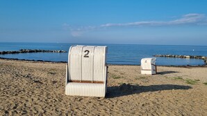Ein Strand mit zwei weißen Liegen mit Nummern, einem sandigen Ufer und einem ruhigen Meer.