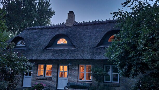 Ein rustikales Haus mit einem Strohdach, vielen Fenstern und einem gepflegten Garten.