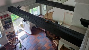 Ein Zimmer mit hohen Decken und sichtbarer Holzbalkenkonstruktion, ein kleines Modell eines Segelbootes und ein Blick ins Freie durch ein Fenster.