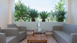 Eine Terrasse mit Korbmöbeln, einem Holztisch und Blick auf viel Grün durch große Fenster.