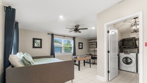 A bedroom with a bed, a ceiling fan, a window with curtains, a foosball table, and a washing machine in the adjacent room. - GameRoom+Dogs+4 BR+Kids+FAST WIFI + 2 Kings (Panama City)