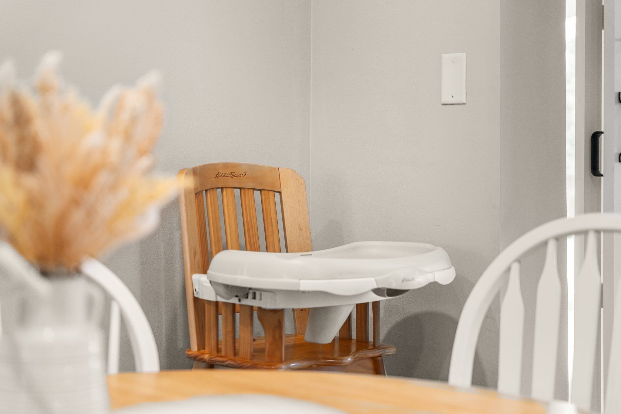 Una silla de madera con asiento y respaldo blancos, una pared blanca y una puerta con manija.