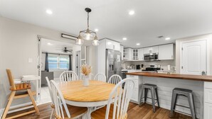 A modern kitchen with white cabinets, a wooden dining table, and bar stools. - GameRoom+Dogs+4 BR+Kids+FAST WIFI + 2 Kings (Panama City)