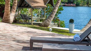 A beachside lounge area with a wooden gazebo, a lounge chair, and a view of the water.