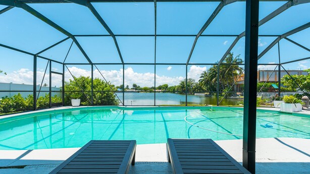 A swimming pool with a view of a lake and palm trees, surrounded by a metal fence and lounge chairs.