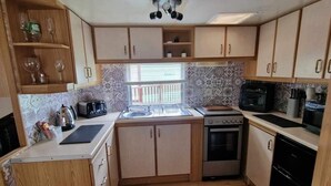 A compact kitchen with wooden cabinets, a built-in oven, a sink, and a microwave. - River Bliss in Whelspool (Welshpool)