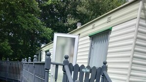A mobile home with a wooden staircase leading to the entrance, surrounded by a metal fence. - River Bliss in Whelspool (Welshpool)