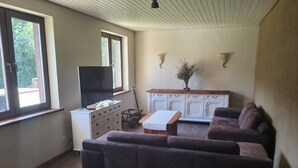 A living room with a large sofa, a television, a cabinet, and a window. - Ferienwohnung am Neetzetal (Thomasburg)