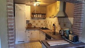 A compact kitchen with white cabinets, a tiled backsplash, and a brick wall. - Ferienwohnung am Neetzetal (Thomasburg)