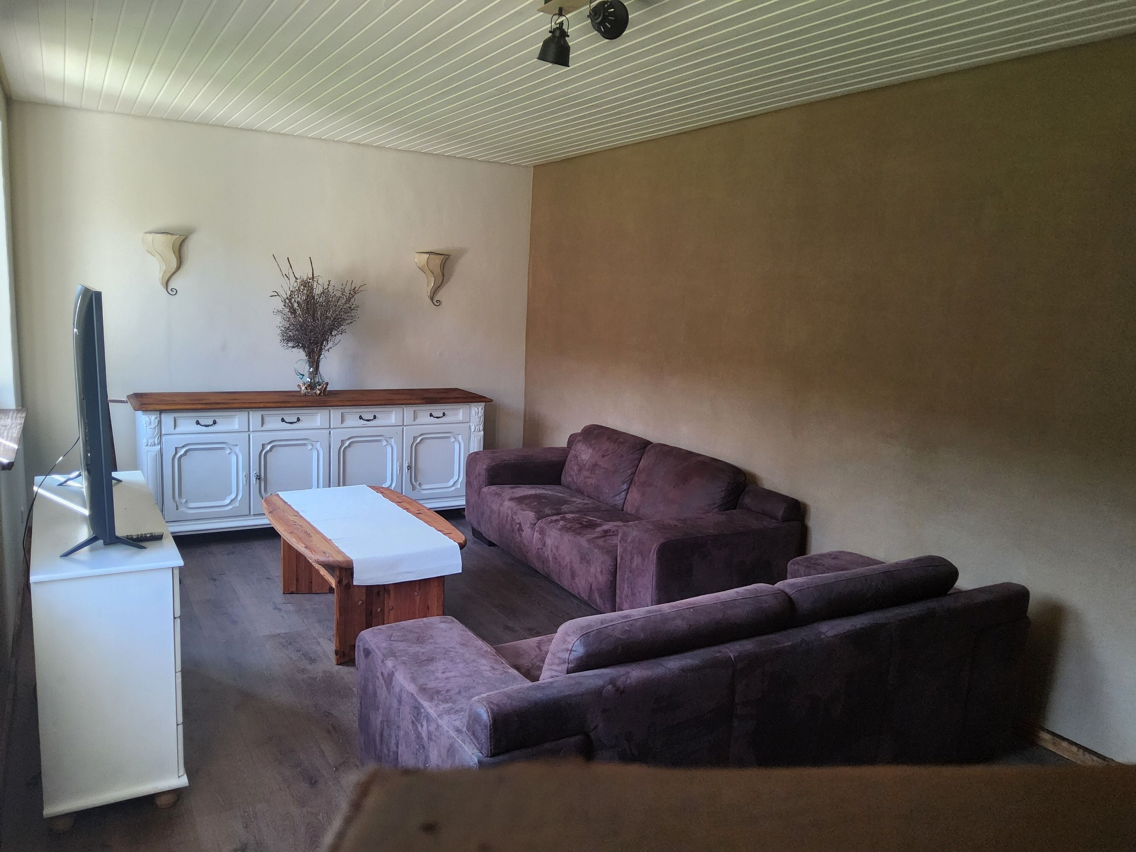 A living room with a purple sofa, a white table, and a TV on a stand.