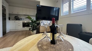 A modern living room with a wooden dining table, a TV, and a kitchen in the background. - SYDNEYS LEADING NO.1 STAY (Coogee)