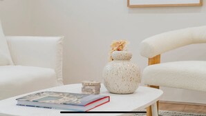 A minimalist living room with a white sofa, a small round table with a book and a decorative vase, and a framed abstract painting on the wall. - SYDNEYS LEADING NO.1 STAY (Coogee)