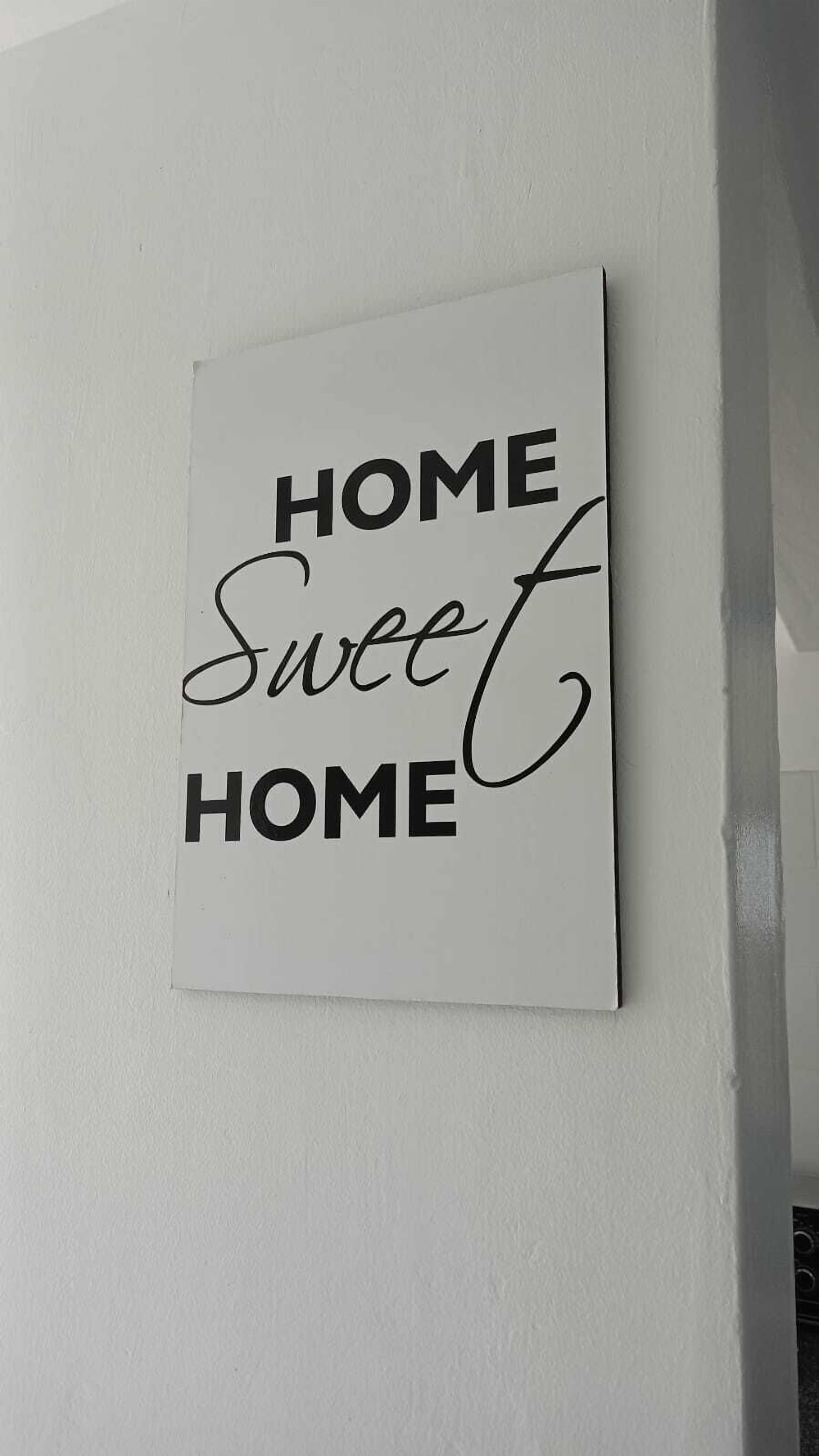 A wall-mounted sign with the text "HOME Sweet HOME" in black and cursive font.