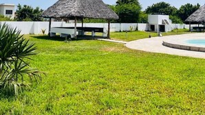 A pool area with thatched-roof structures and a grassy lawn. - Kijani Residences Condos (Malindi)