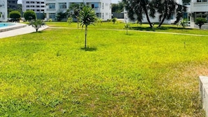 A grassy area with palm trees and white buildings with multiple floors and balconies. - Kijani Residences Condos (Malindi)
