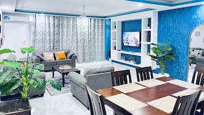 A modern living room with a grey sofa, a coffee table, and a TV mounted on a blue accent wall. - Kijani Residences Condos (Malindi)