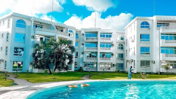 A modern hotel with a swimming pool, featuring a clear blue sky and white buildings. - Kijani Residences Condos (Malindi)