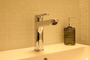 A bathroom with a chrome faucet and a soap dispenser on a white sink. - Union Apartment 4 (Belp)