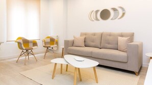 A modern living room with a beige sofa, two matching armchairs, a small white coffee table, and a wall-mounted circular mirror set.