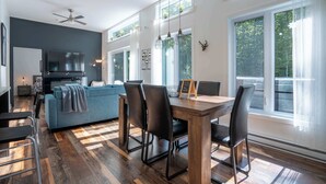 A modern kitchen with a built-in oven, a dining area with a wooden table and chairs, and large windows with a view of greenery. - Absolute comfort with Spa | Chalet le Petit Castor (Chertsey)
