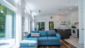 A modern living room with a large window, a blue sofa, and a wooden floor. - Absolute comfort with Spa | Chalet le Petit Castor (Chertsey)