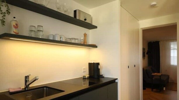 Una cucina moderna con un piano di lavoro nero, lavello in acciaio inossidabile ed scaffali a parete con utensili da cucina.