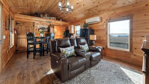 A wooden cabin interior with a leather sofa, dining table, and chairs. - Valley View Cottage (Omaha)
