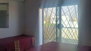 Ein Zimmer mit einem Bett, einem kleinen Tisch und einem Fenster mit Blick auf ein Gebäude.