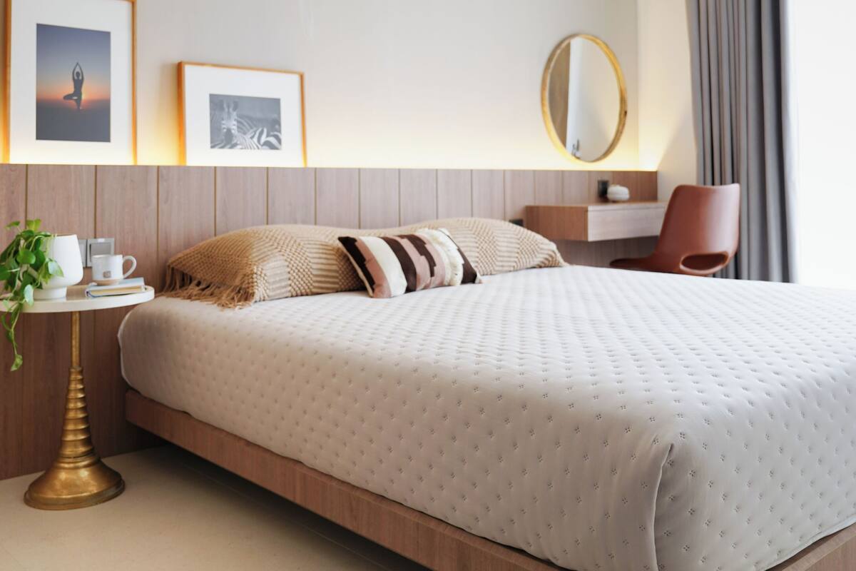 A modern hotel room with a large bed, bedside table, and a chair.