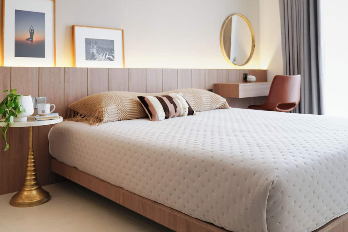 A modern hotel room with a large bed, bedside table, and a chair.