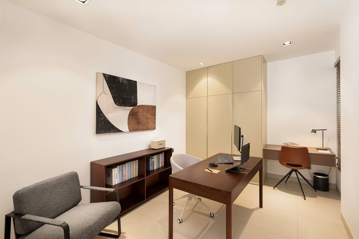 A modern office with a desk, chair, bookshelf, and a large mirror.