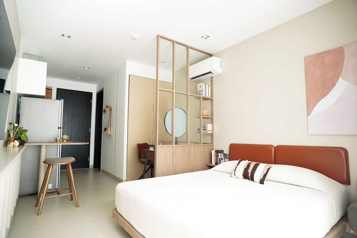 A modern hotel room with a bed, a desk, a chair, a bookshelf, and a wall-mounted air conditioner.