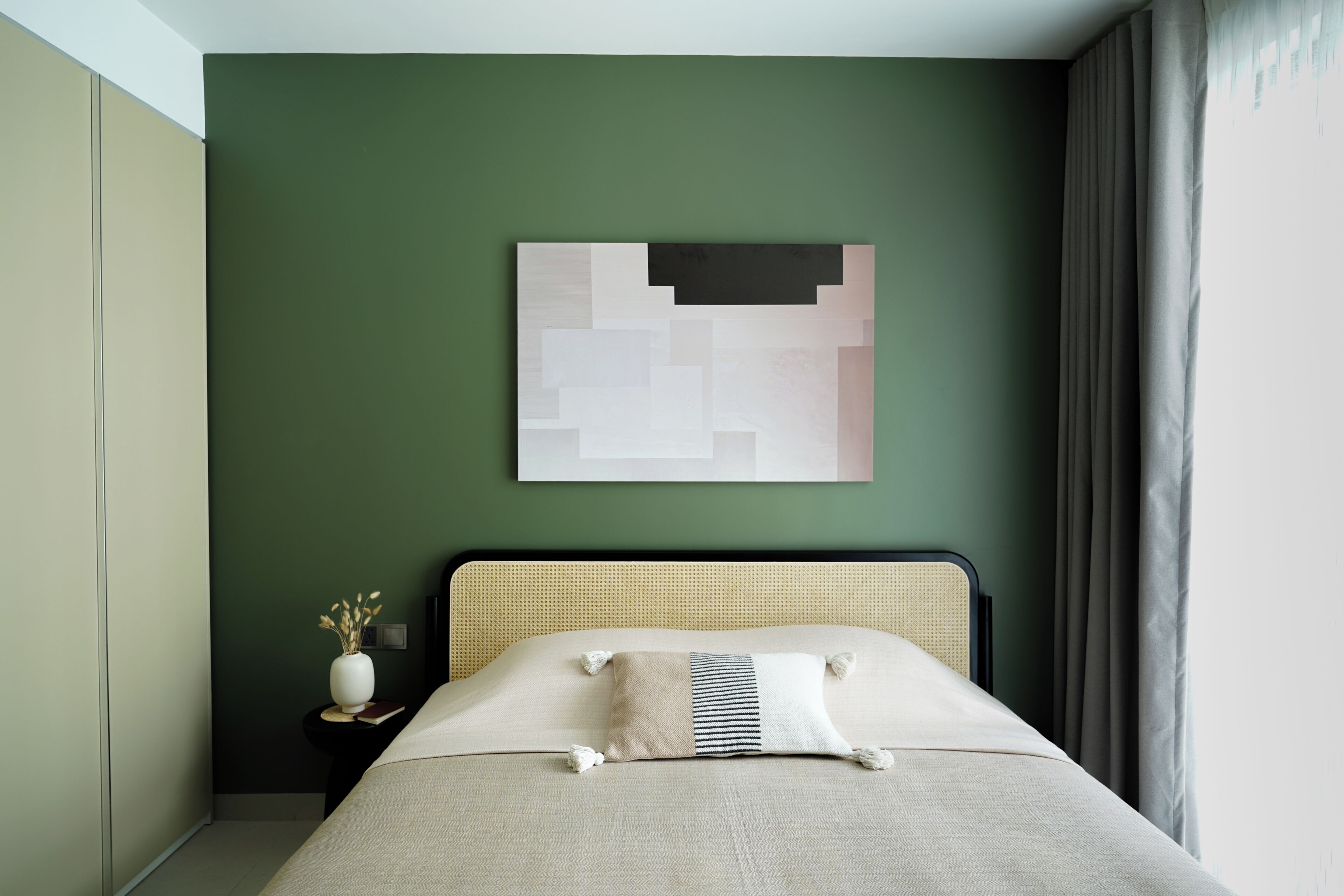 A bed with a headboard, a wall-mounted abstract artwork, a bedside table with a vase, and a window with curtains.