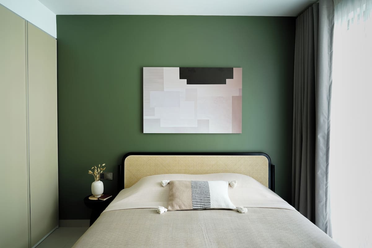 A bed with a headboard, a wall-mounted abstract artwork, a bedside table with a vase, and a window with curtains.
