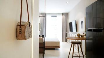 A modern hotel room with a bed, a small kitchenette, a TV, and a wicker bag hanging on the wall.