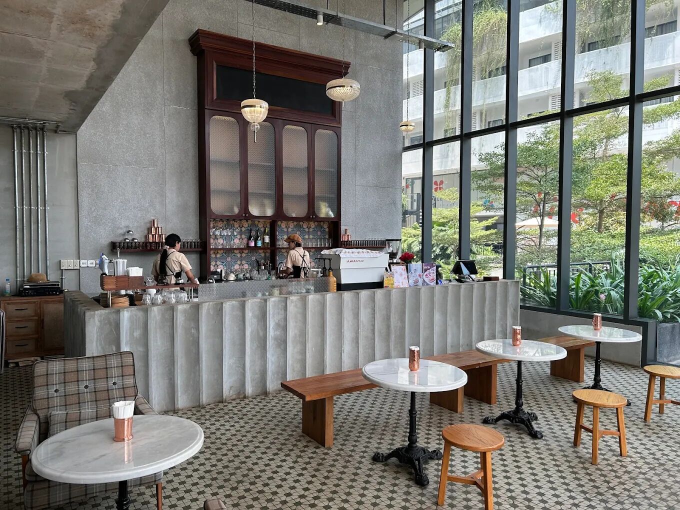 Ein modernes Café mit Barbereich, runden Tischen und Blick auf Grünflächen.
