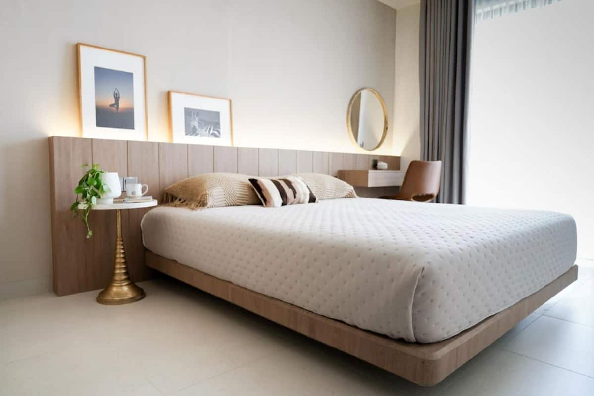 A modern hotel room with a minimalist design, featuring a large bed, a bedside table with a lamp, and framed pictures on the wall.