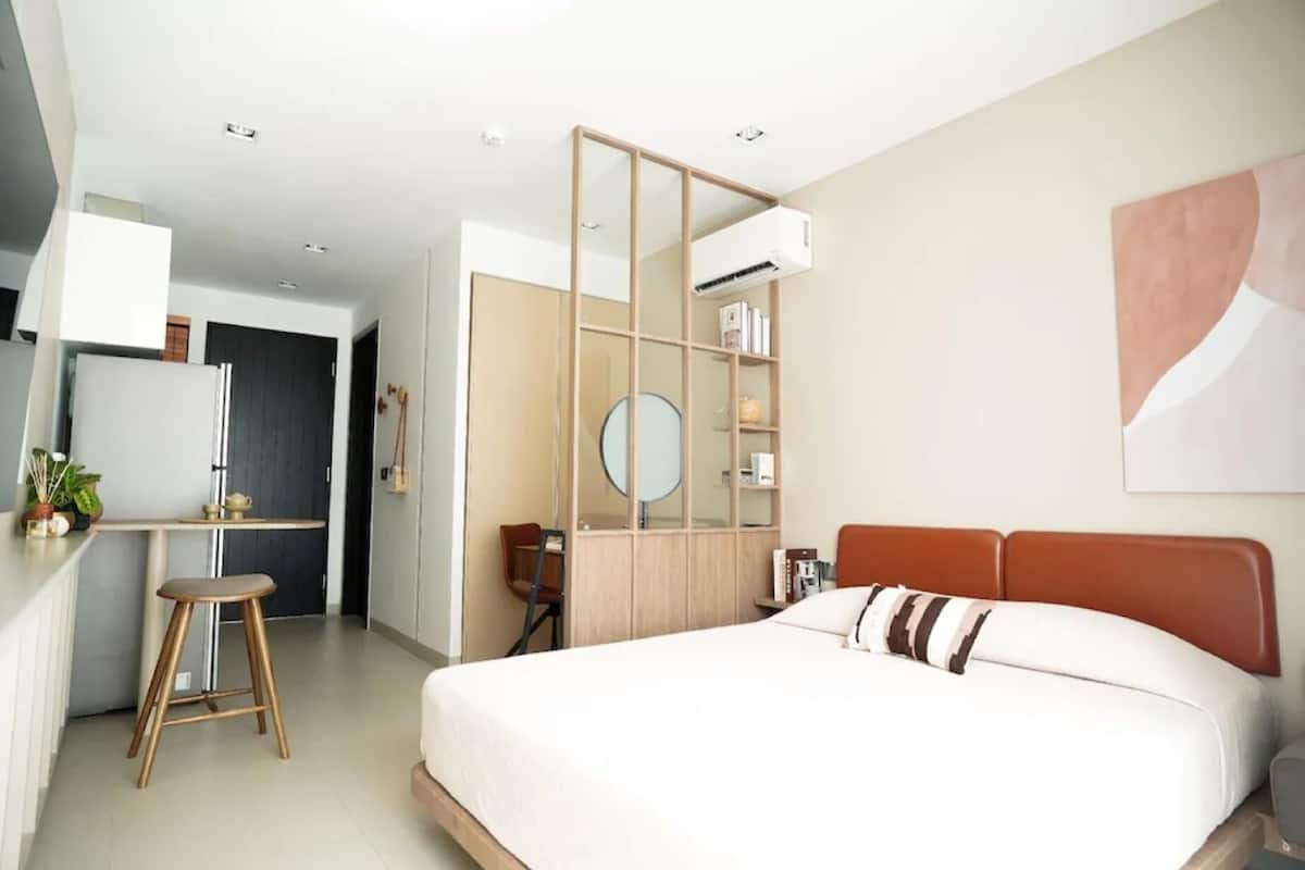 A modern hotel room with a bed, a desk, a chair, a mirror, and a bookshelf.